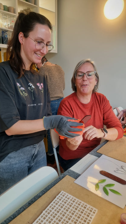 Twee vrouwen glimlachen tijdens een glas in lood bloemenworkshop bij Maak Atelier in Antwerpen.