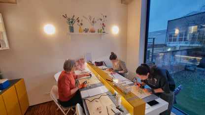 Drie vrouwen maken handgemaakte glas in lood bloemen tijdens Tiffany workshop in atelier.